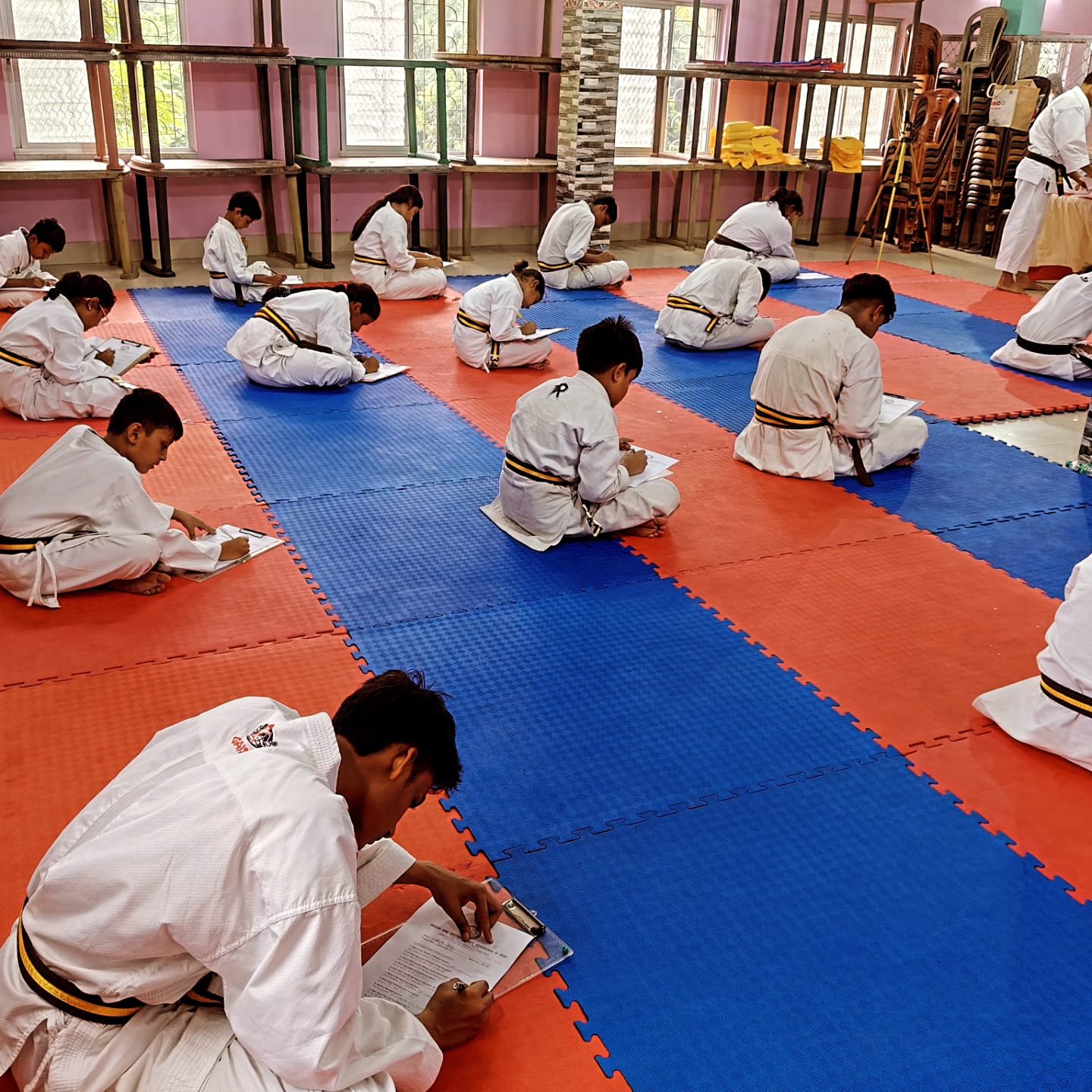 Students continuing the written black belt exam, seated on the mat